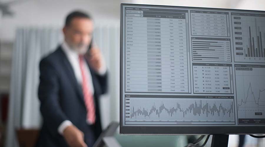 Man on phone with trading graphs on a computer